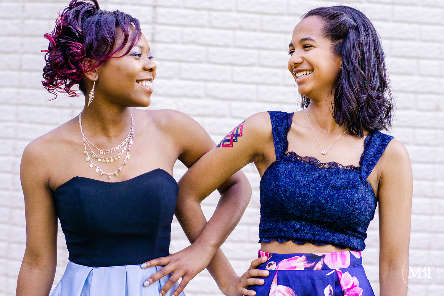 best friends smiling & looking at each other with their arms linked, taken on their prom night at a backyard in Fairfax, Virginia taken by a Northern Virginia portrait photographer
