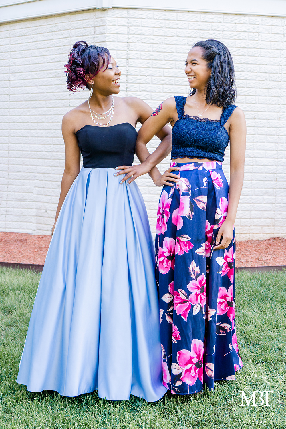 best friends smiling & looking at each other with their arms linked, taken on their prom night at a backyard in Fairfax, Virginia taken by a Northern Virginia portrait photographer
