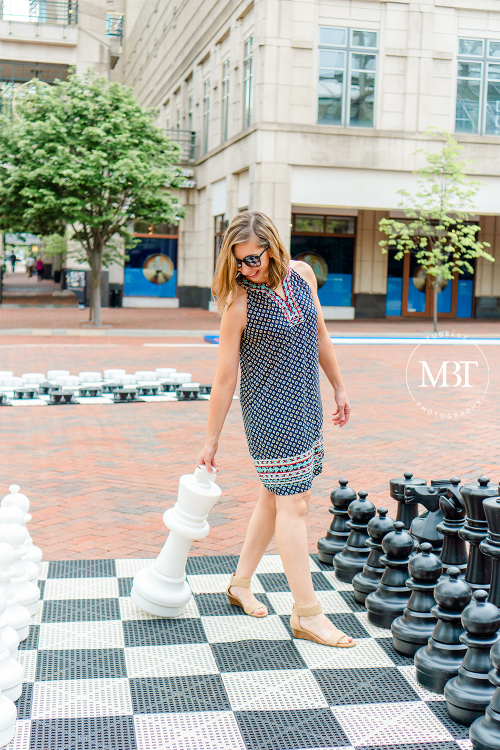 lifestyle session - woman wearing a printed embroidered dress lugging around a chess piece on a giant chess board taken at Reston, Virginia by a lifestyle photographer in Virginia