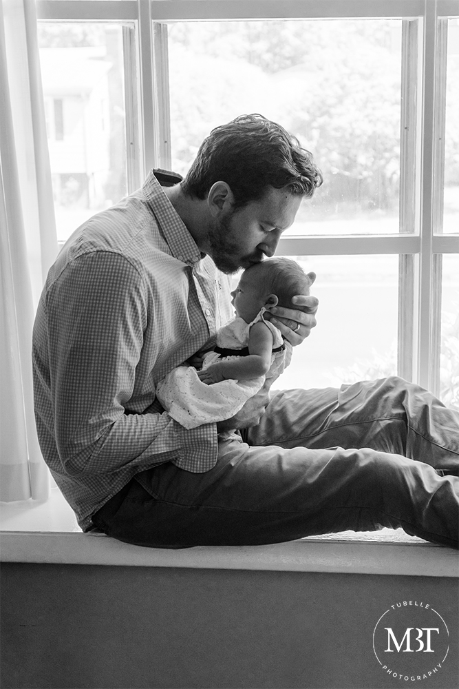 daddy kissing newborn baby girl by the window during their newborn session in Alexandria, Virginia by a Virginia lifestyle newborn photographer