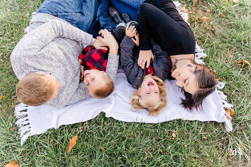 family of 4 laughing while laying on the grass during their family session in Fairfax, Virginia by a DMV family photographer