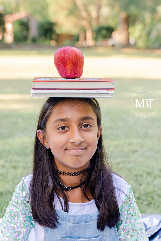 school aged girl with a book and apple on her head during her back to school session in Arlington, Virginia by a Washington, DC children's photographer