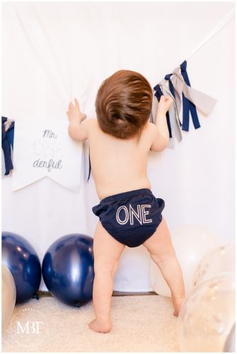 baby boy playing wearing a One underwear during a cake smash session in Fairfax, Virginia by a Virginia cake smash photographer