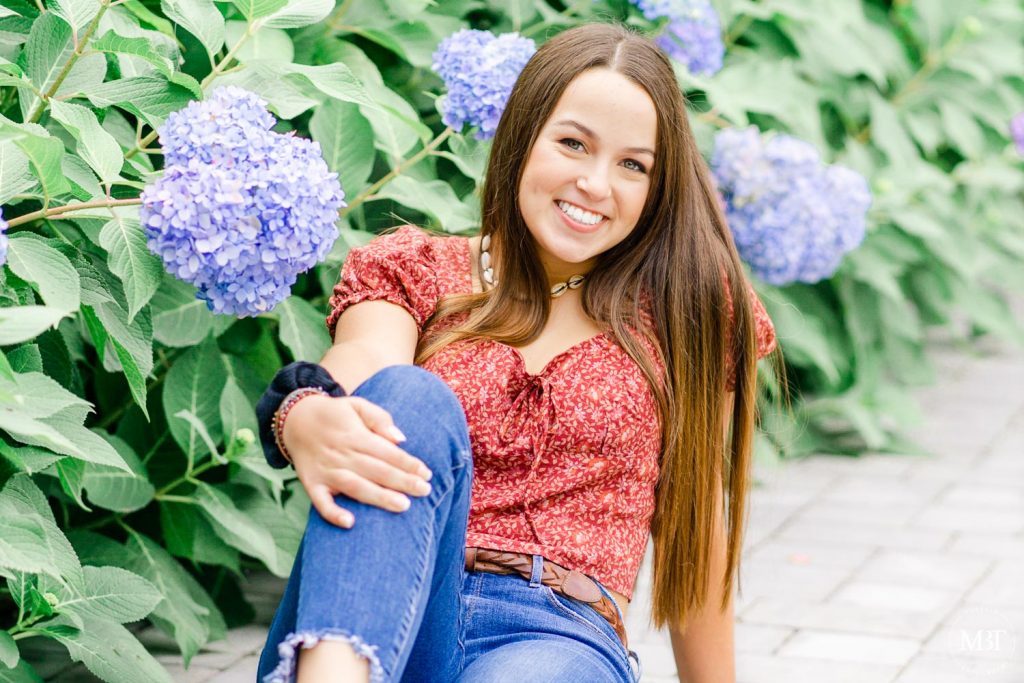 girl sitting by the hydrangeas during a senior session in Airlie taken by a Northern Virginia senior photographer