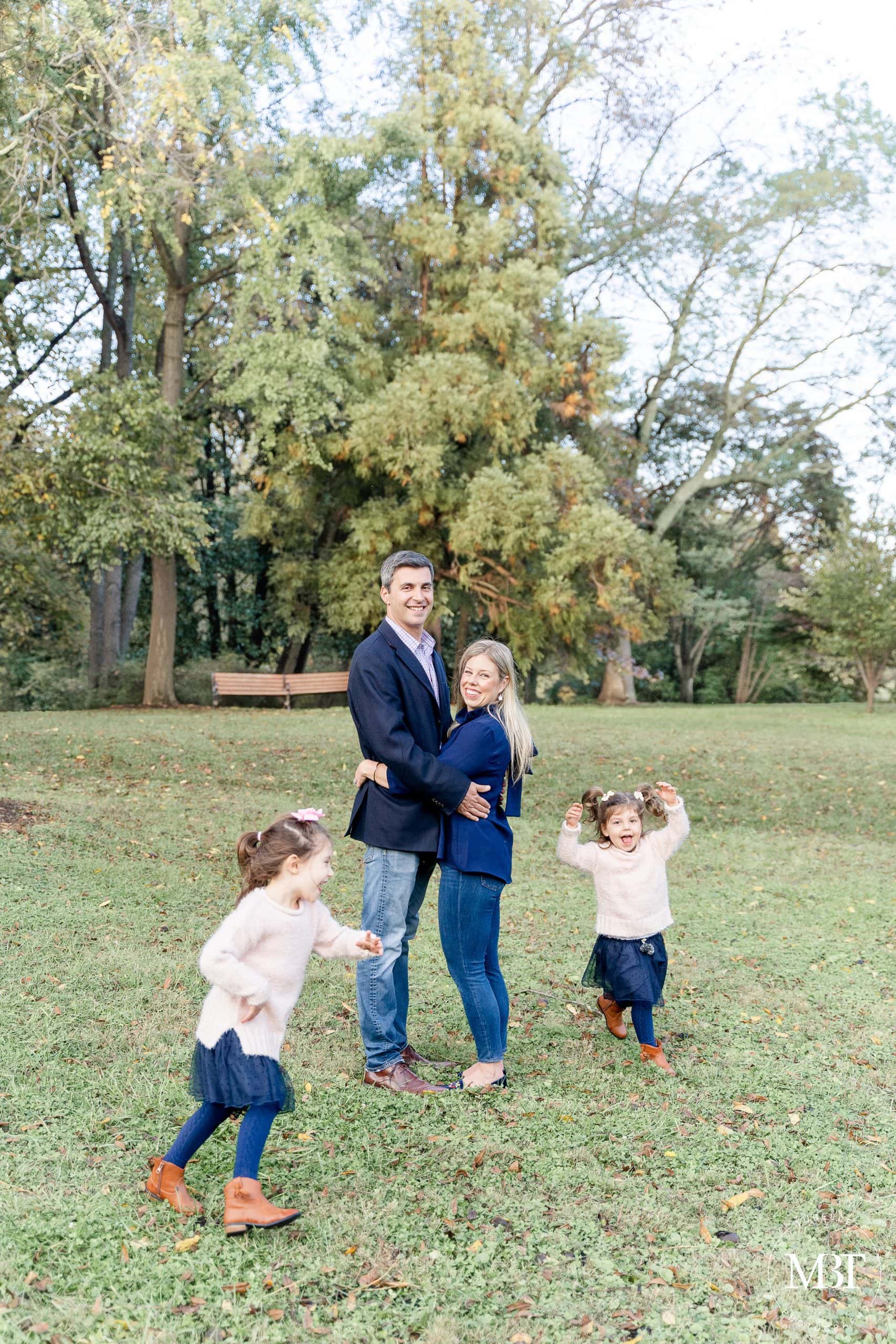 mom & dad hugging each other while the girls are running around in circle, taken in Falls Church - Virginia family photography