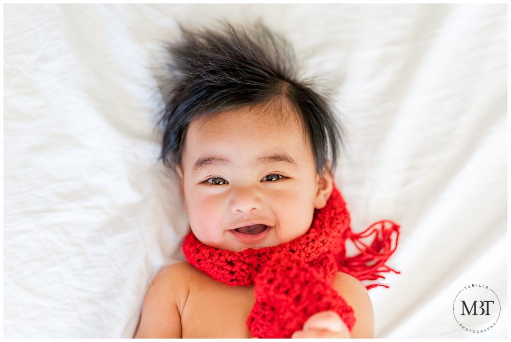baby boy wearing a red scarf smirking during his milestone baby photo shoot in Mclean, Virginia by TuBelle Photography, a baby photographer in Northern Virginia