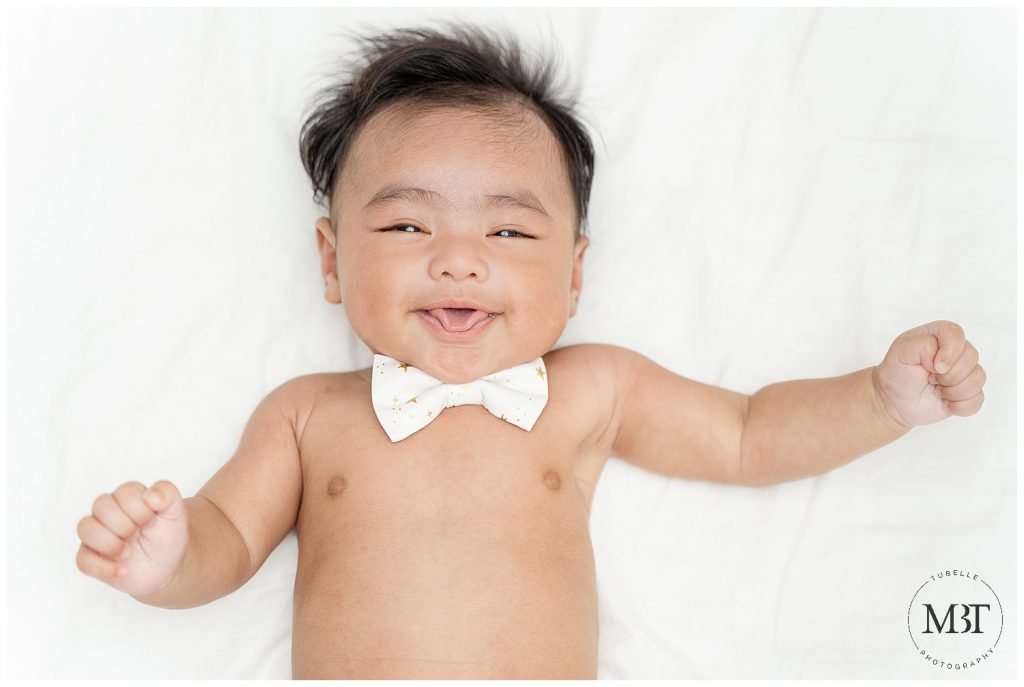 baby boy smiling with his tongue out wearing a bow tie during his milestone baby photo shoot in Mclean, Virginia by TuBelle Photography, a baby photographer in Virginia