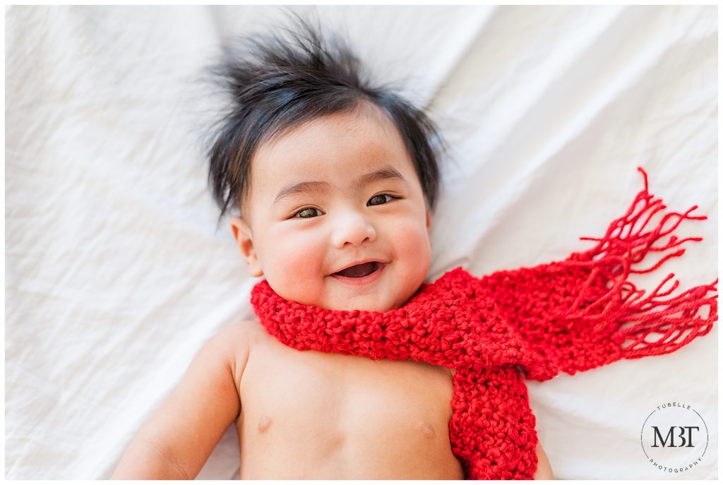 baby boy wearing a red scarf smiling during his milestone baby photo shoot in Mclean, Virginia by TuBelle Photography, a baby photographer in Virginia