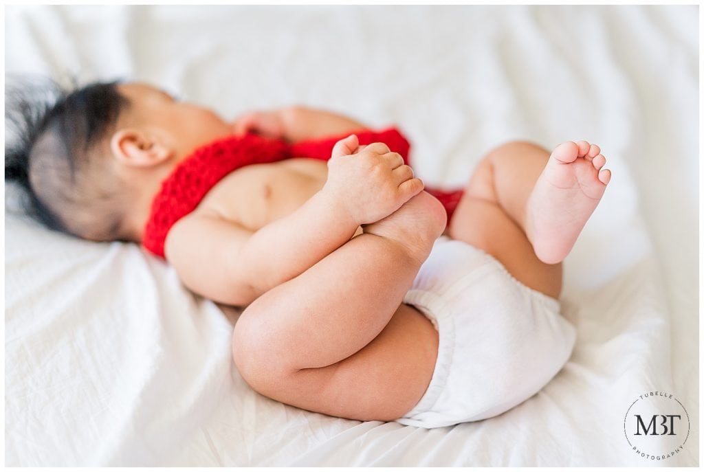 baby boy wearing a red scarf playing with his foot during his milestone baby photo shoot in Mclean, Virginia by TuBelle Photography, a baby photographer in Virginia
