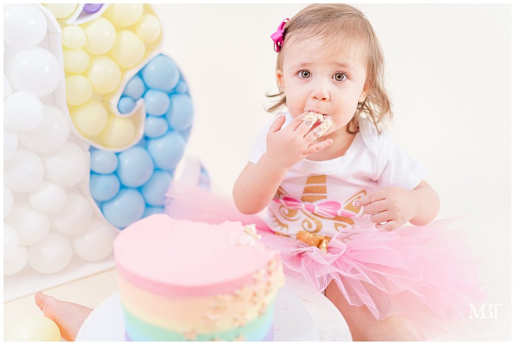 girl eating cake during cake smash session in Gainesville, Virginia taken by TuBelle Photography, a Prince William County cake smash photographer