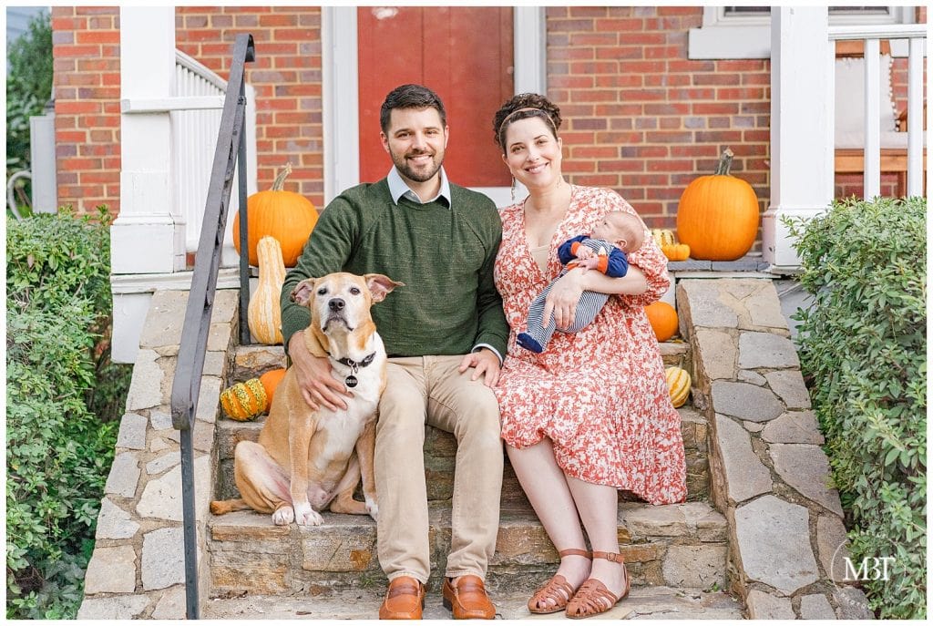 Mom, Dad, Newborn Baby Boy and Family Dog sitting on front porch smiling at the camera for their lifestyle newborn session. Taken by TuBelle Photography, a NoVa lifestyle photographer.