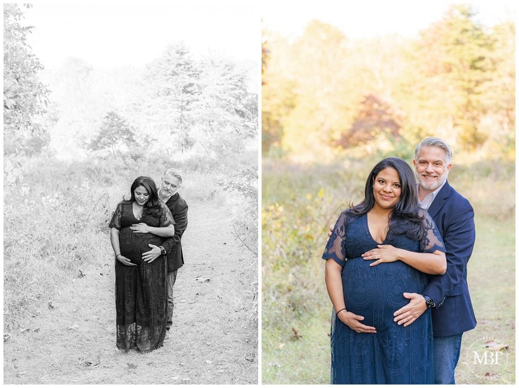 Expecting couple in navy wardrobe wrap arms around baby bump at their maternity photos during fall minis in Chantilly, Virginia. Taken by TuBelle Photography, a NoVa Photographer.