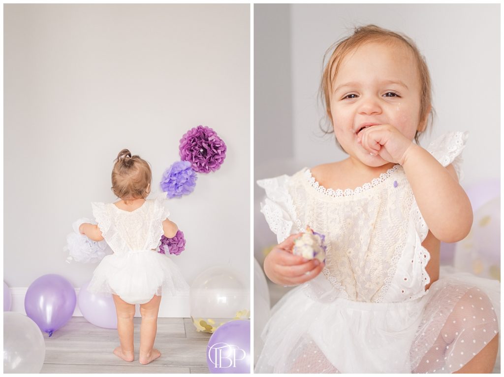 Little girl in beige onesie looking at white and purple balloons and flowers for cake smash session in Haymarket, Virginia. Taken by TuBelle Photography, a Fairfax County, Virginia cake smash photographer. 