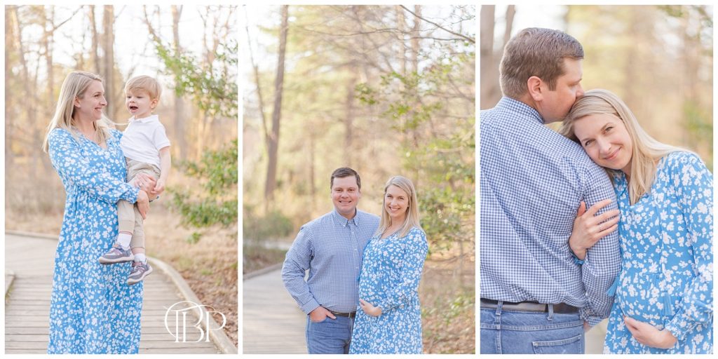 Expecting mom in blue floral dress holding son, mom and dad embracing and family of three walking on park bridge at their maternity session in Alexandria, VA. Taken by TuBelle Photography, a Fairfax County, Virginia maternity photographer.