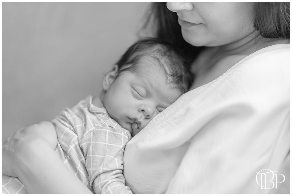 Black and white photo of mom holding newborn baby boy on her chest for their living room newborn pictures in Fairfax County, VA. Taken by TuBelle Photography, a Newborn Photographer.