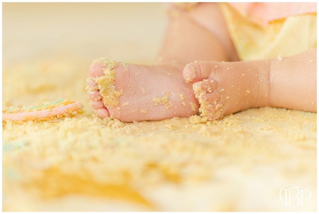 Baby girl's feet covered in cake crumbs for her rainbow themed cake smash photos in Fairfax County, Virginia. Taken by TuBelle Photography, a Fairfax County, VA Cake Smash Photographer.