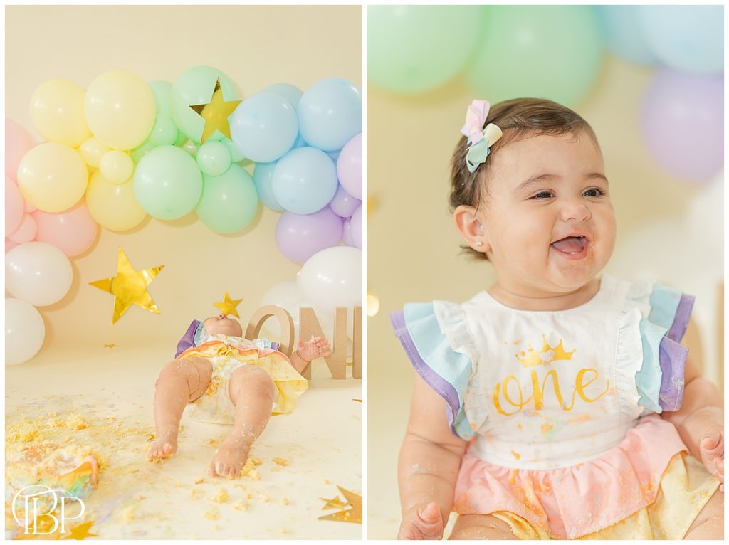 Baby girl smiling and laying in the floor for her cake smash pictures. Taken by TuBelle Photography, a Fairfax County, Virginia cake smash photographer.