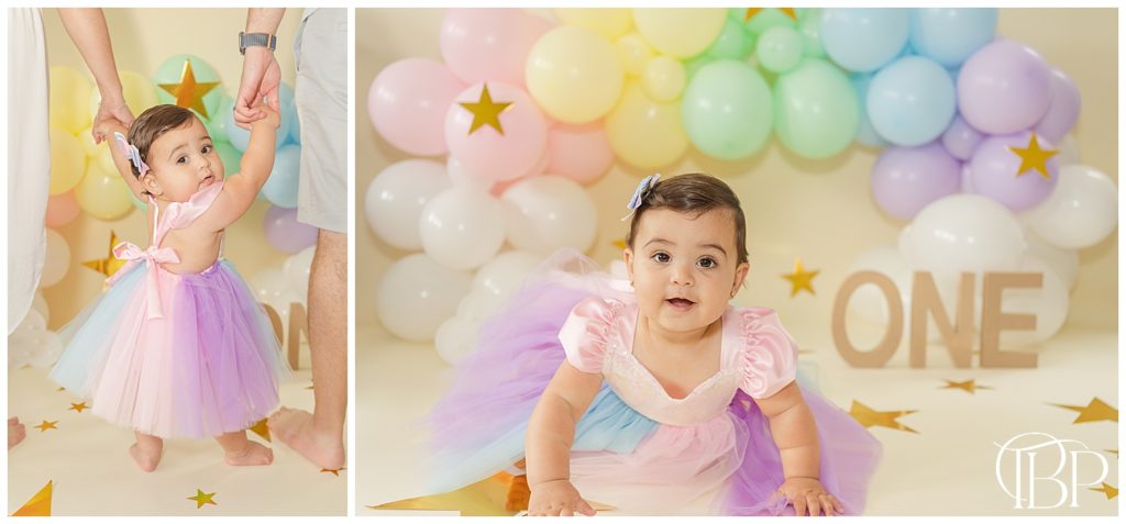 Baby girl in colorful tutu sitting in front of a rainbow balloon arch for her rainbow themed cake smash pictures in Fairfax County, Virginia. Taken by TuBelle Photography, a cake smash photographer.
