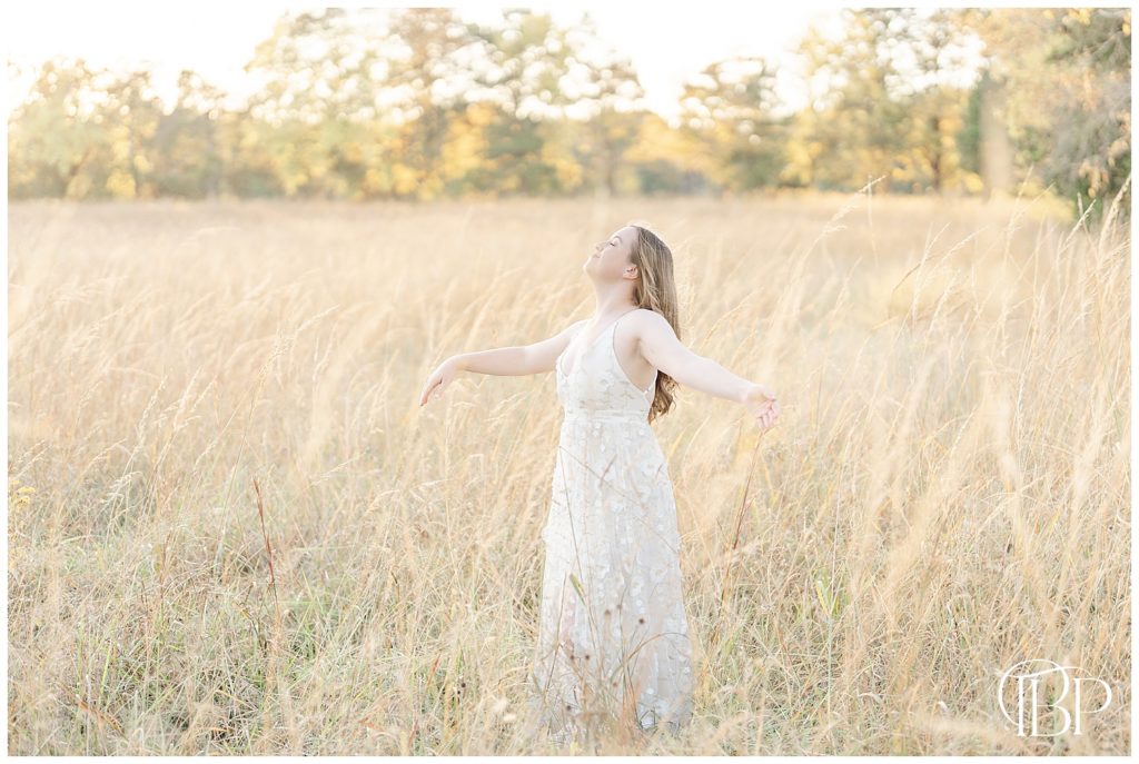 girl soaking in everything in the middle of a field with tall grass taken by a Manassas, Virginia senior photographer