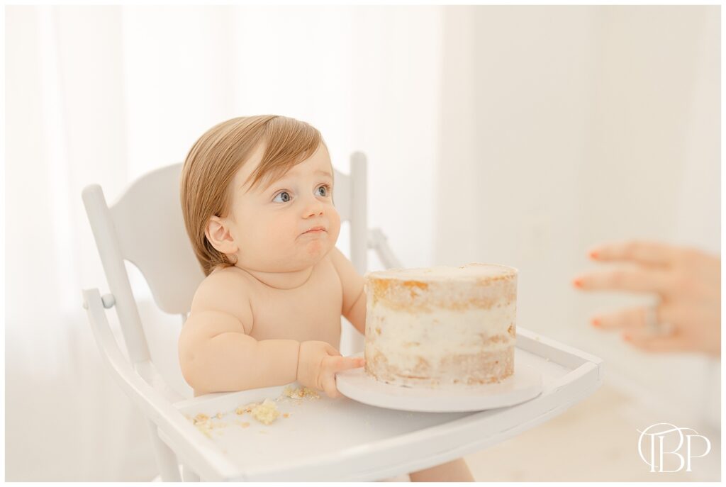 Baby handing cake to mom during simple cake smash pictures in Ashburn, Virginia