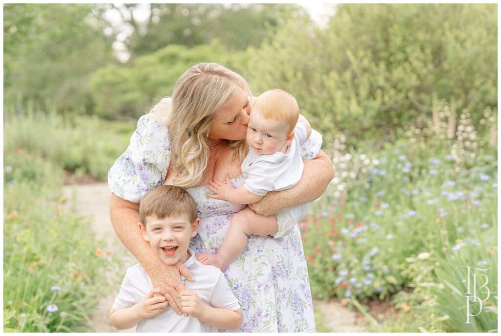 Mom kissing baby, brother with big smile